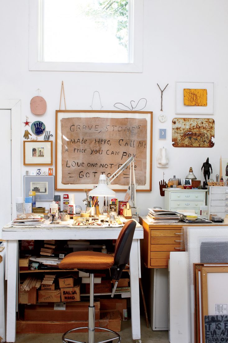 Framed above the artist's desk, a handwritten sign advertises the services of a gravestone maker.