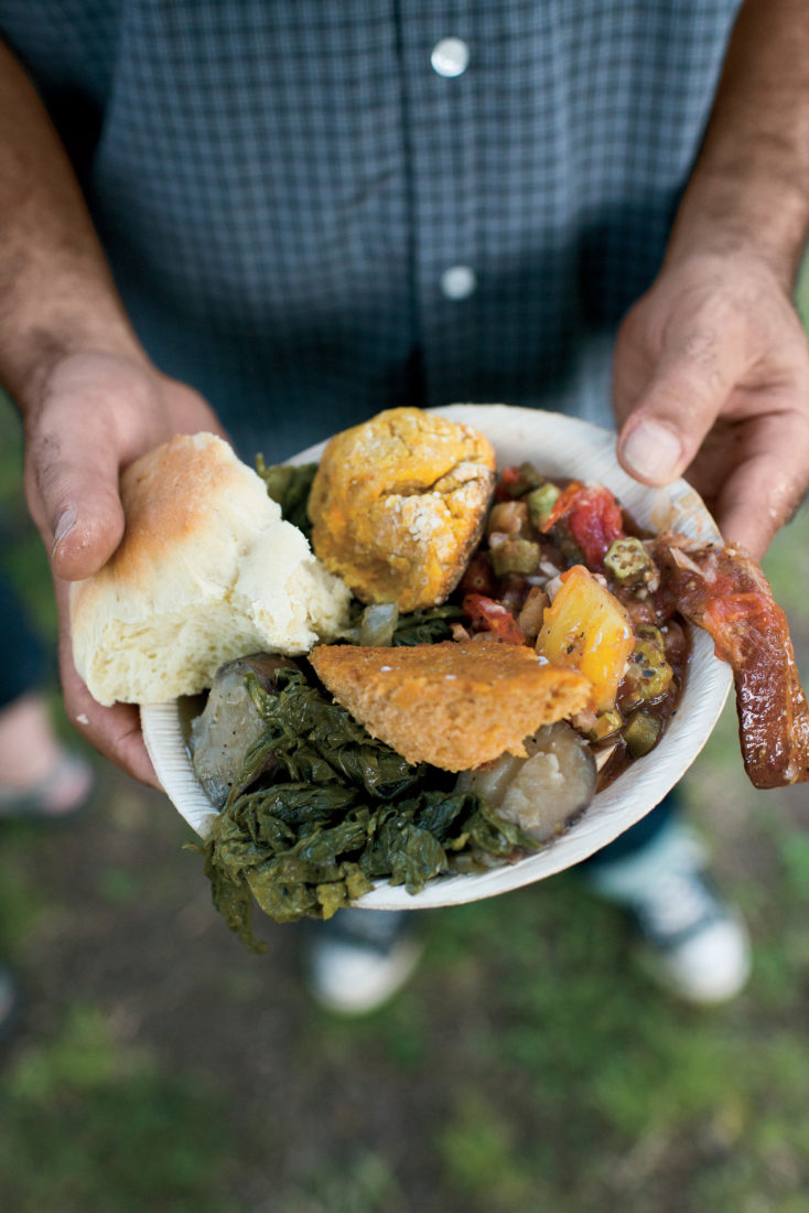 A guest holds a plate of sweet potato pone, okra stew, greens, and more.