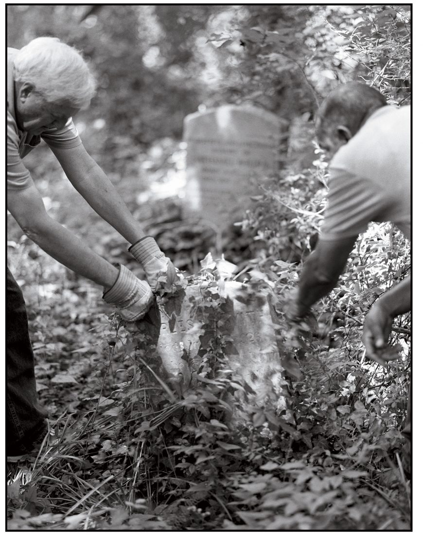 John Shuck (Left) and Marvin Harris strip English ivy from a grave marker in Evergreen.