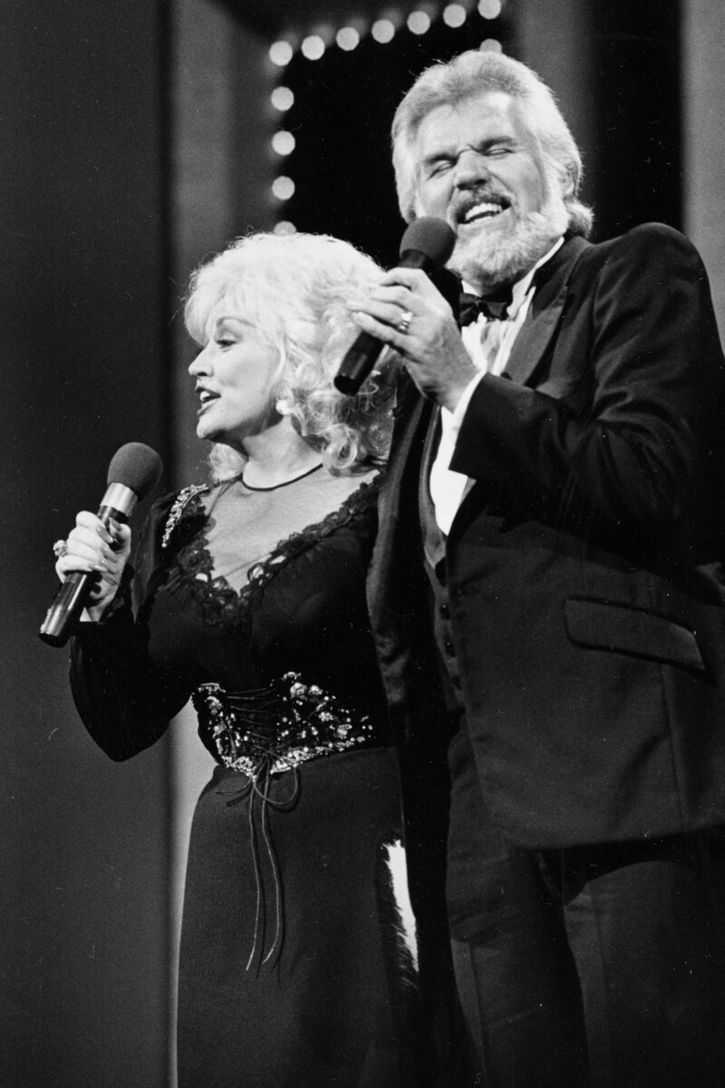 Dolly Parton and Kenny Rogers on stage singing into microphones