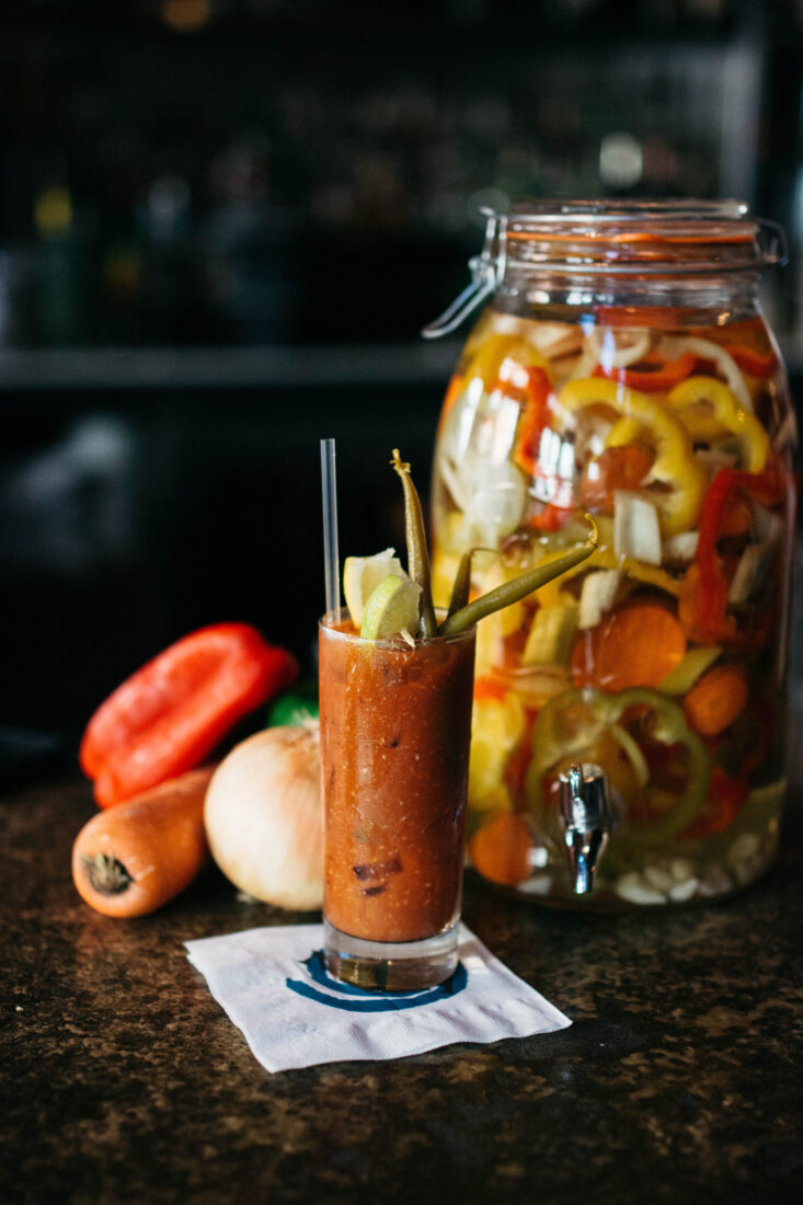 A Bloody Mary in front of a jar of pickled peppers.