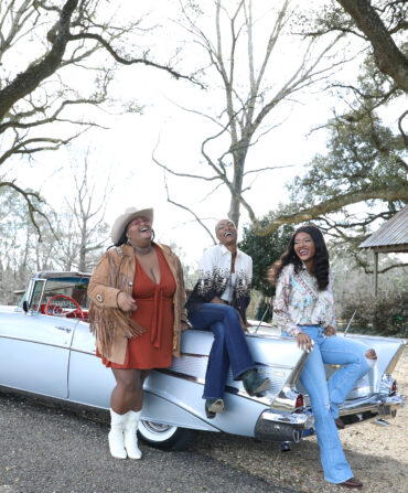 Three woman sit on a vintage car, laughing