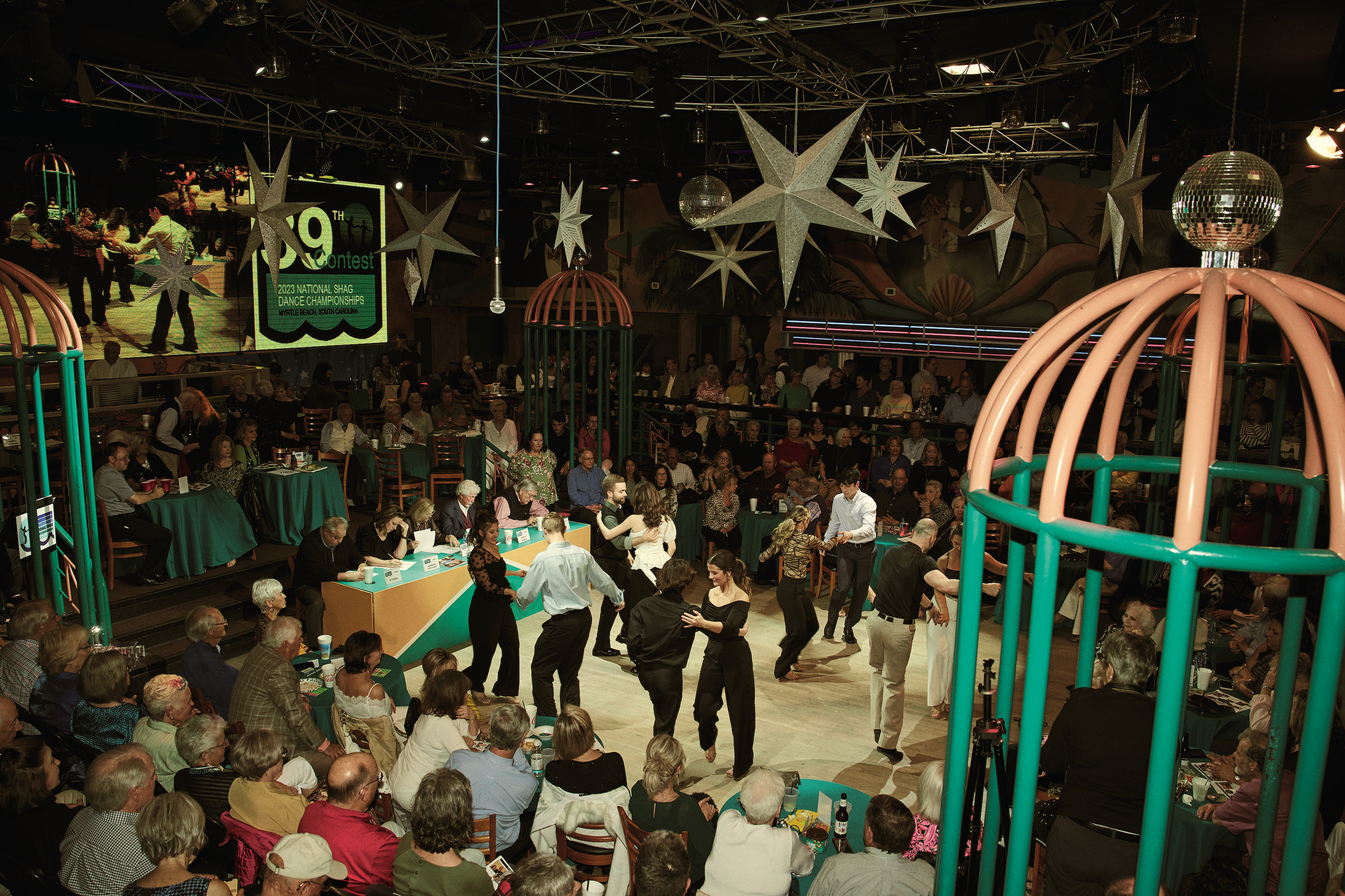 A dancing competition in a room with dancers on the floor; paper stars hang above the floor