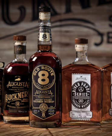A lineup of five bottles of bourbon on a wood cask top