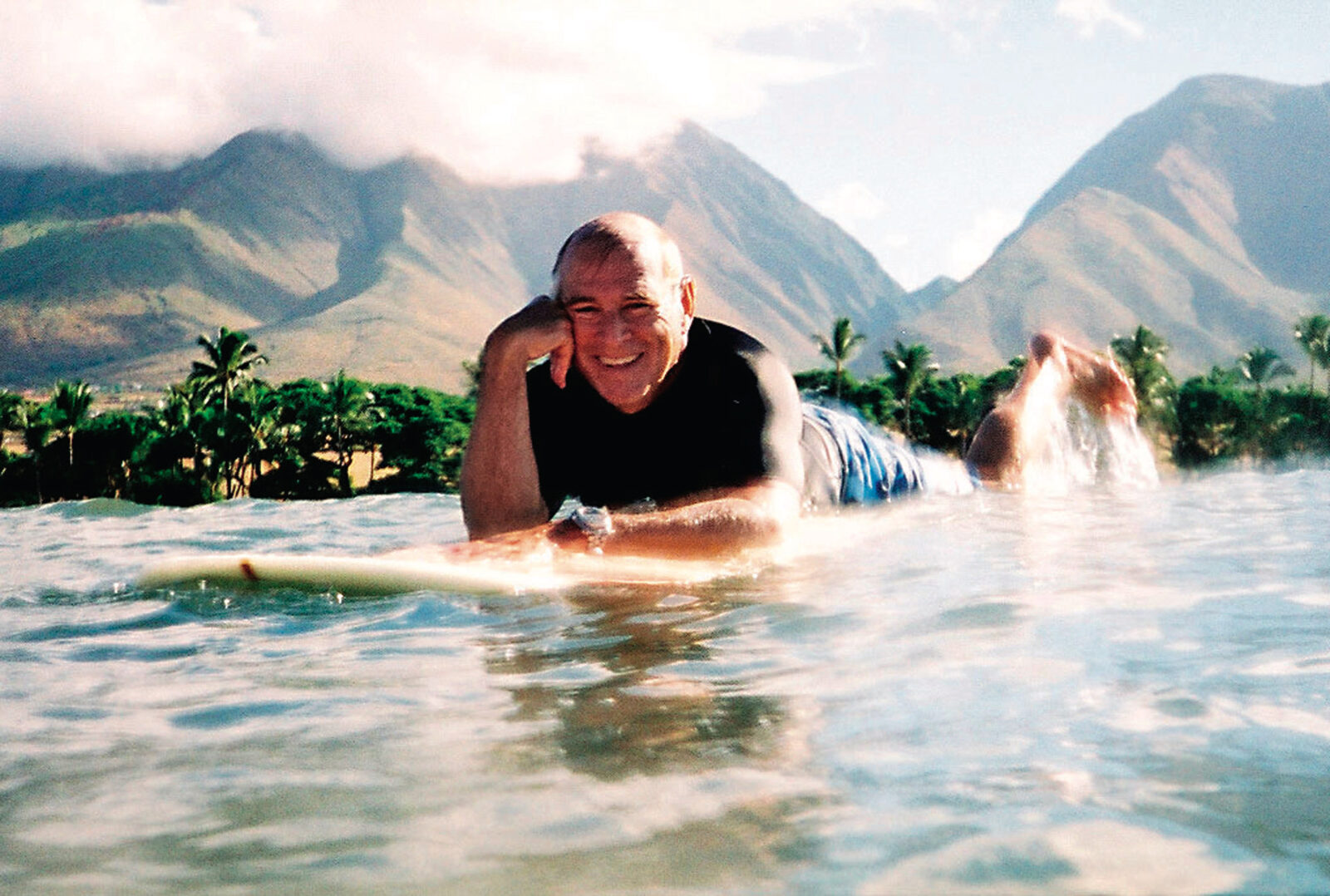 Buffett smiles while laying in the water on a board