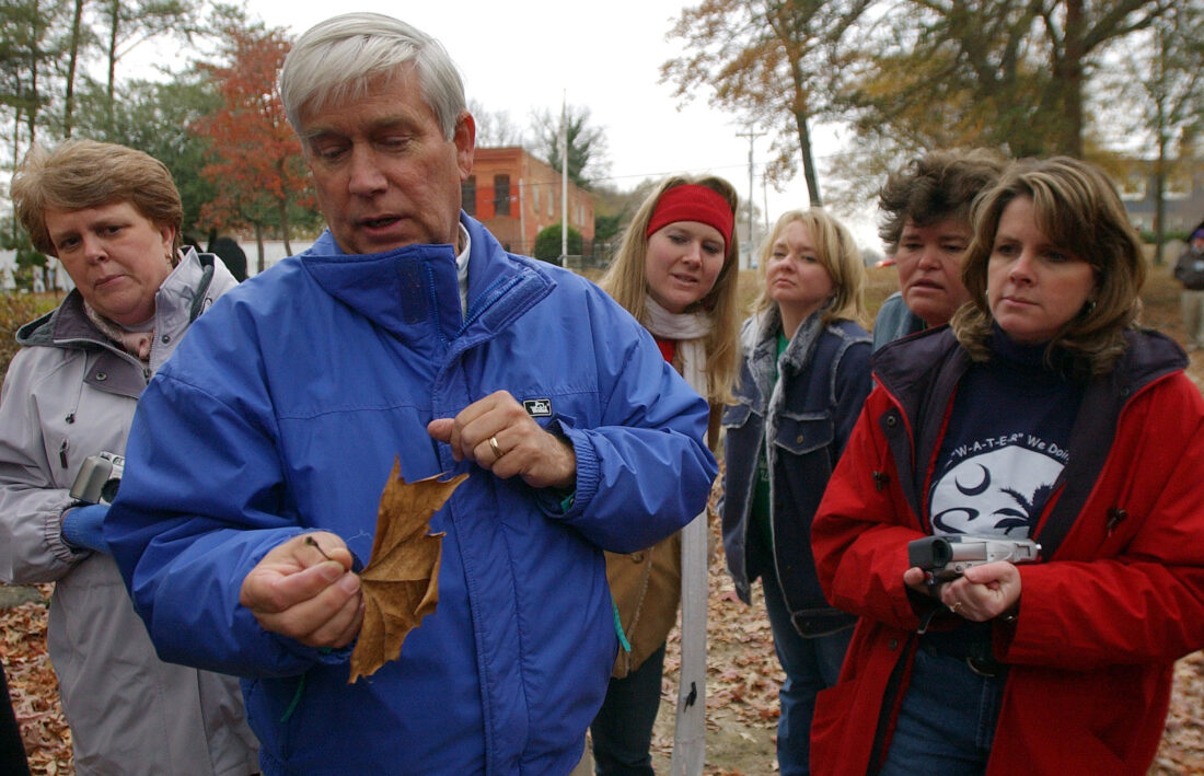 An older man holds a leaf with children behind him