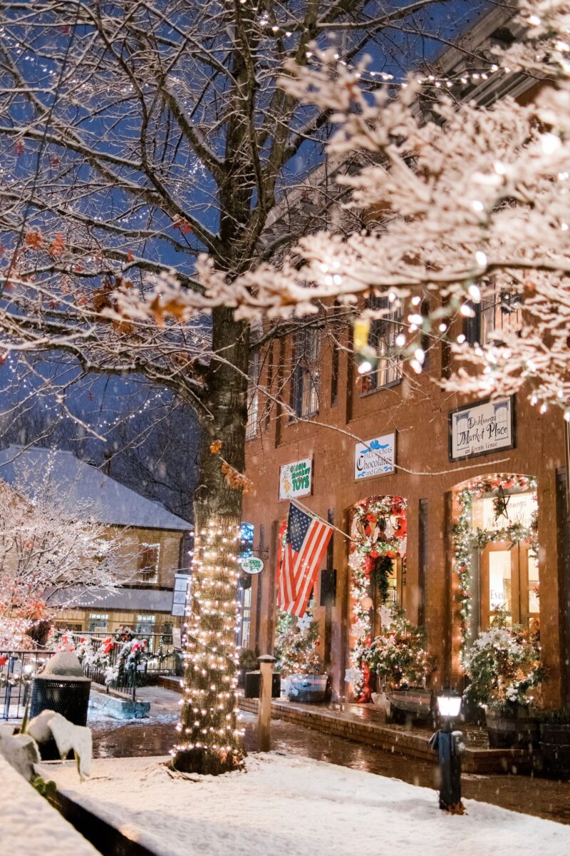 A brick building with shops and Christmas decor and lights in the snow