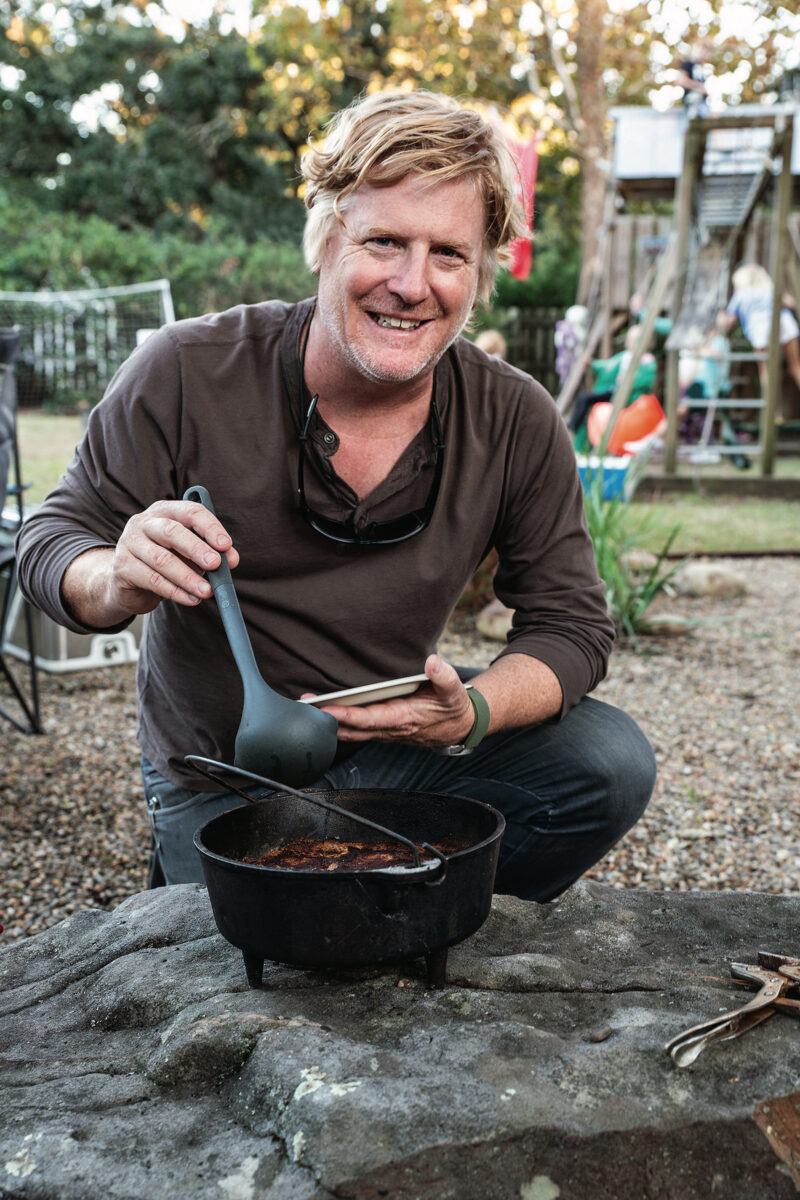 A man crouches in a backyard with a cast-iron pot of cobbler