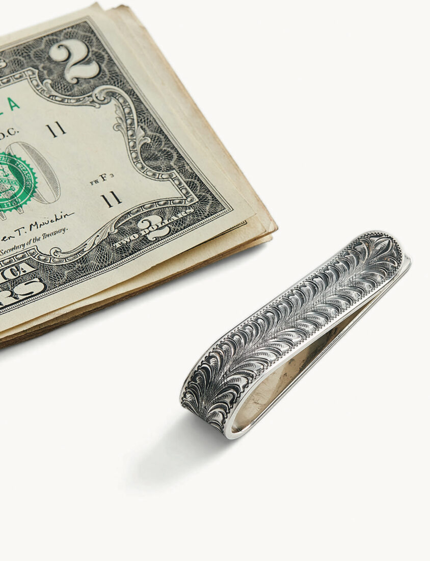 A silver patterned money clip with a two dollar bill above it