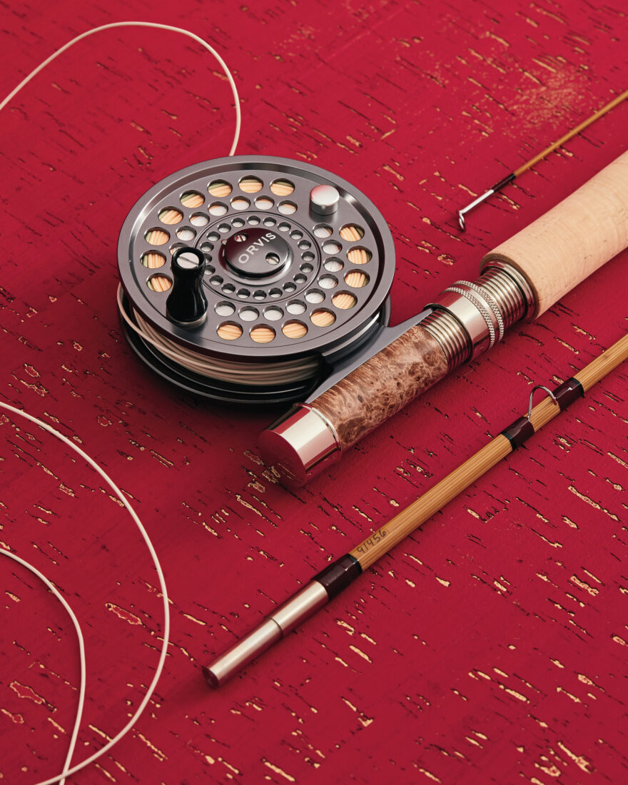 A part of a flyfishing rod and reel on a red and gold background