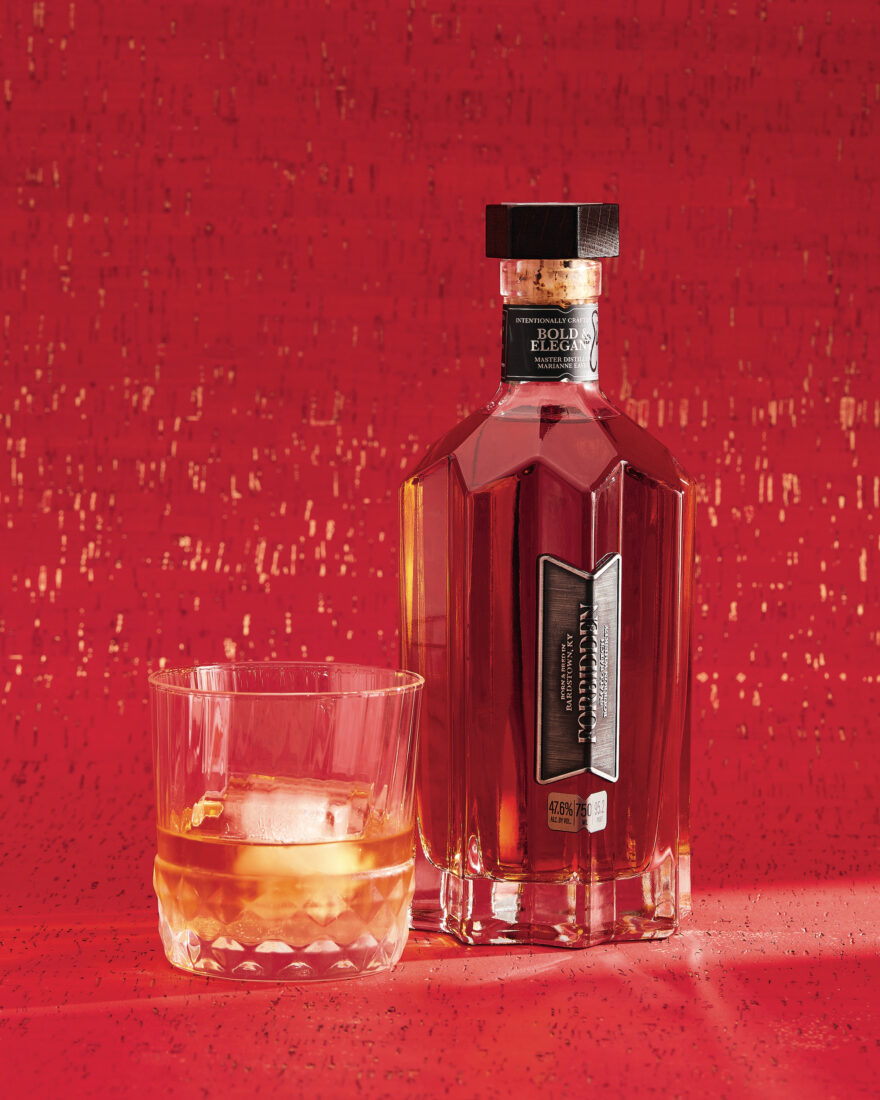 A bottle of bourbon with a filled rocks glass on a red backrgound