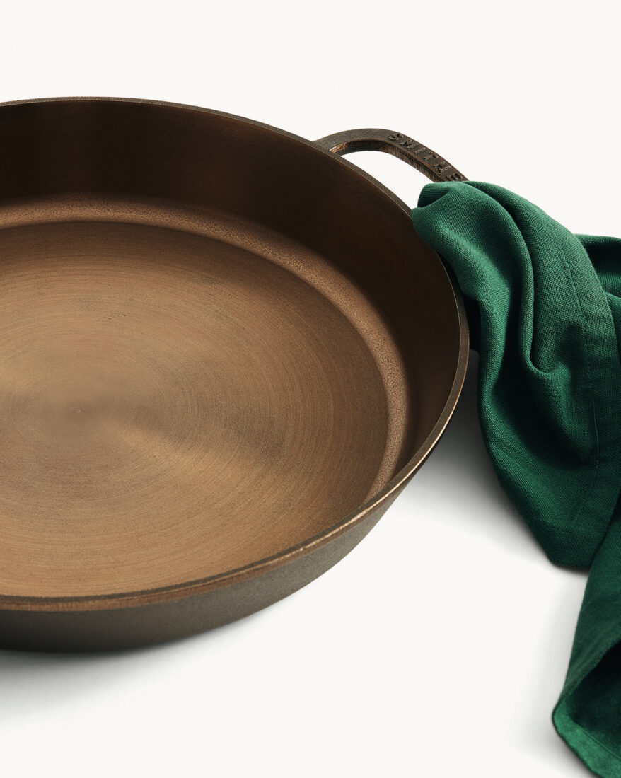 A part of a cast-iron pan with a green towel wrapped around the handle