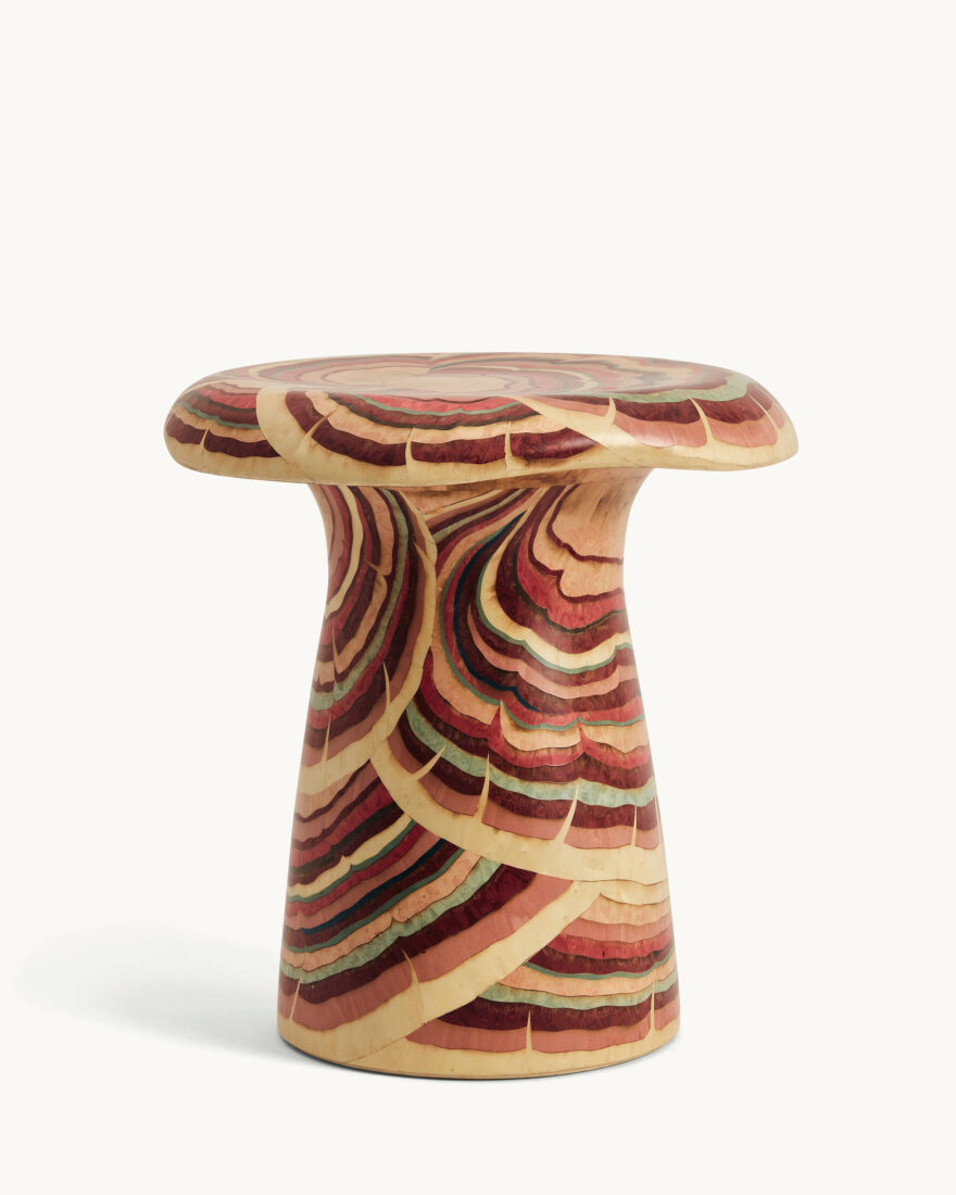 A mushroom-shaped stool with red, dark brown, and green wood marbled throughout