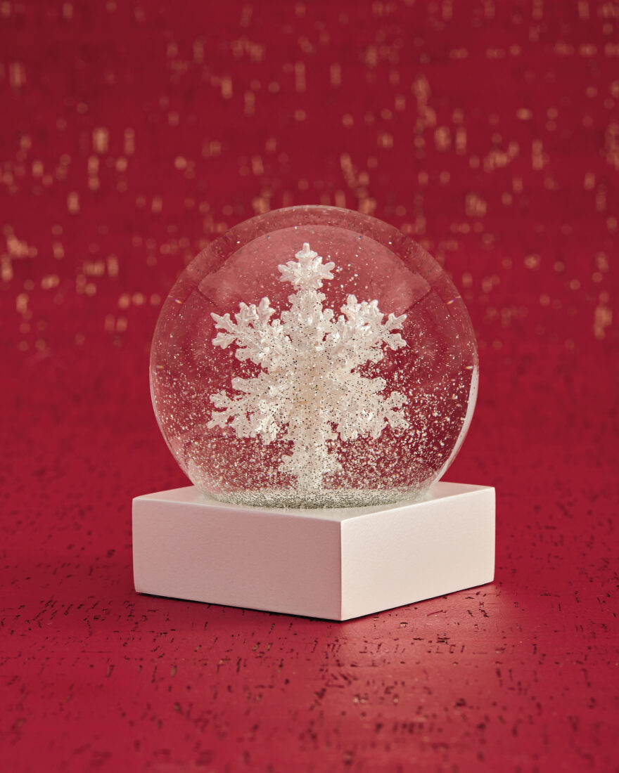 A snow globe with a large sculptural snowflake within the glass. The globe is on a red background with a snow-like pattern of white