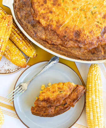 A slice of corn casserole on a plate with the larger casserole above