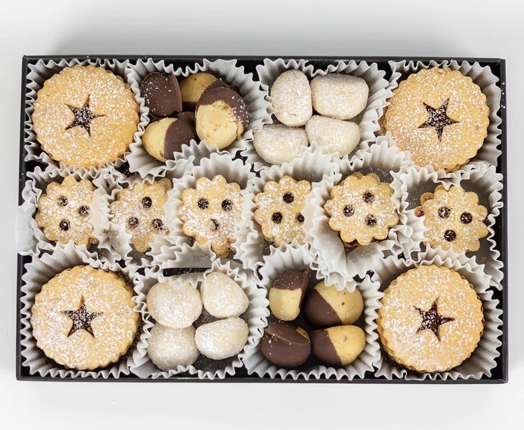 A box of holiday cookies with white wrappers, dusted with sugar and imprinted with star and dot designs