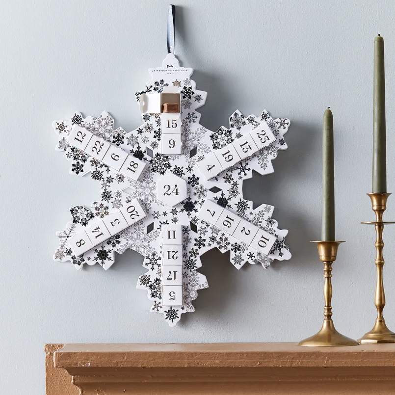 A snowflake-shaped advent calendar with black and grey printed snowflakes and boxes with numbers