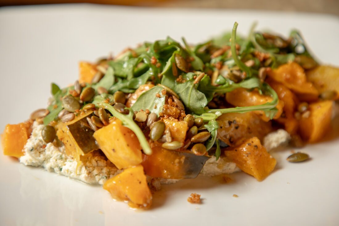 A close-up of roasted squash on a plate. The squash is on top of whipped mascarpone and has arugula and a brown dressing on top