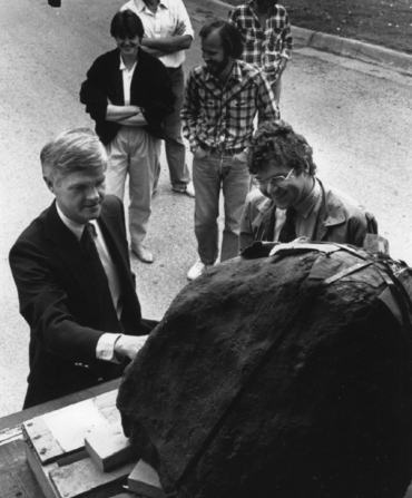 A black and white image of a group of men in suits approaching the meteorite at the University of Arkansas.