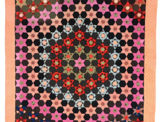 A hexagon-patterned quilt with black, pink, red, green, and light blue fabric on a lighter orange border.
