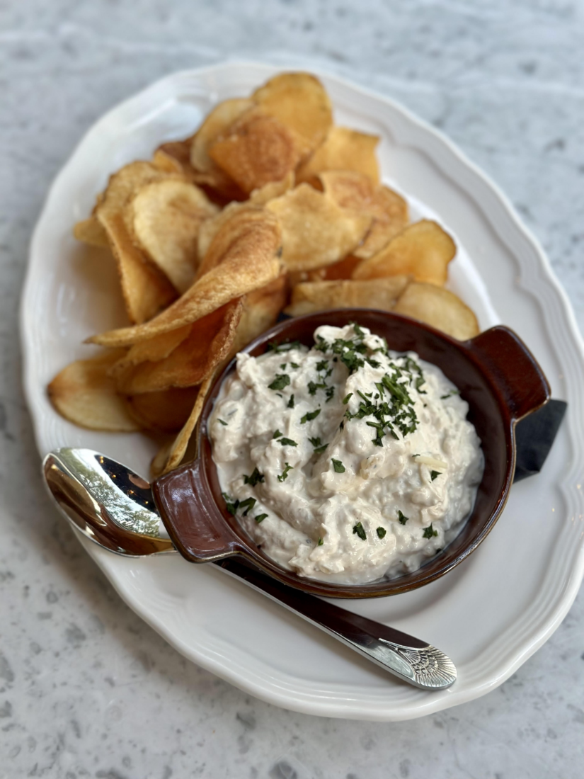A white platter holds potato chips, a spoon, and a small dish with a creamy dip inside.