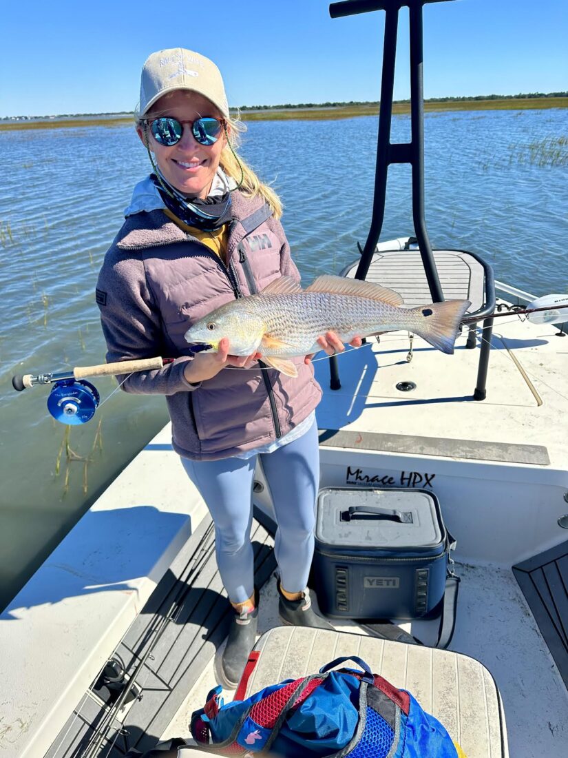 A woman holds a redfish while standing on a boat