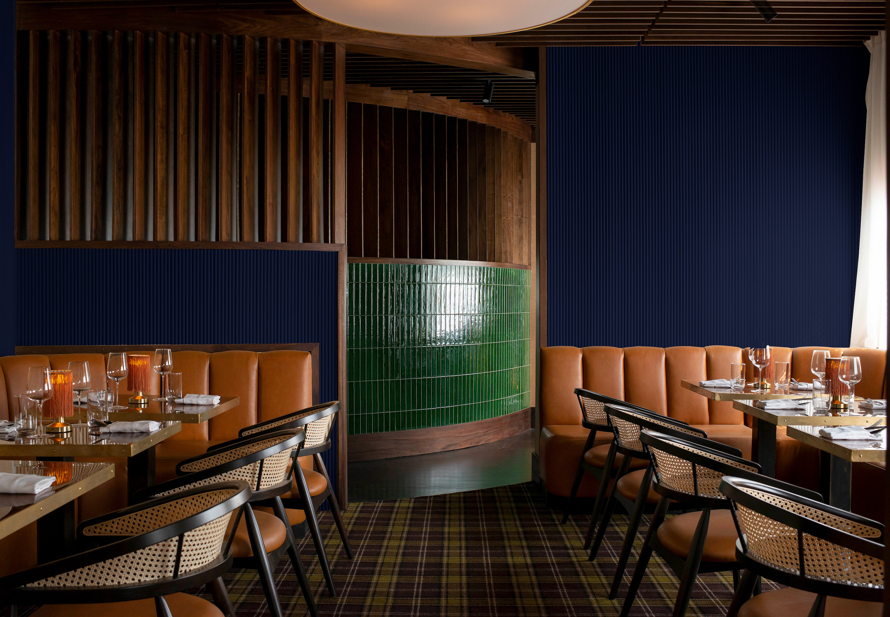 A dining room in a restaurant. It has tan booths, a dark blue wall, wood detailing, and green tile