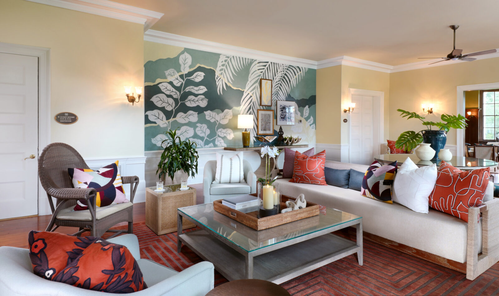 The inside of a guestroom with a couch, candle, coffee table, and painted mural wall with leaves