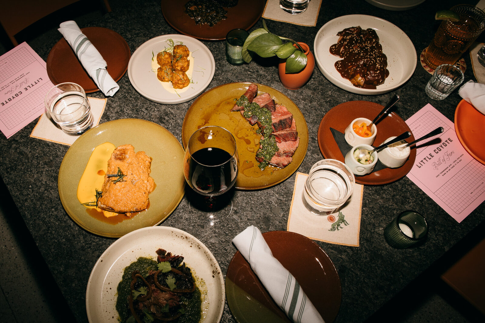 A spread of plates on a table with smoked meats, dips, and a glass of wine