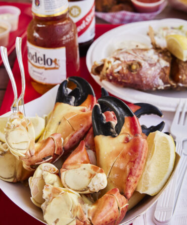 Stone Crab Claws and whole fried Lane Snapper on a red table with beer