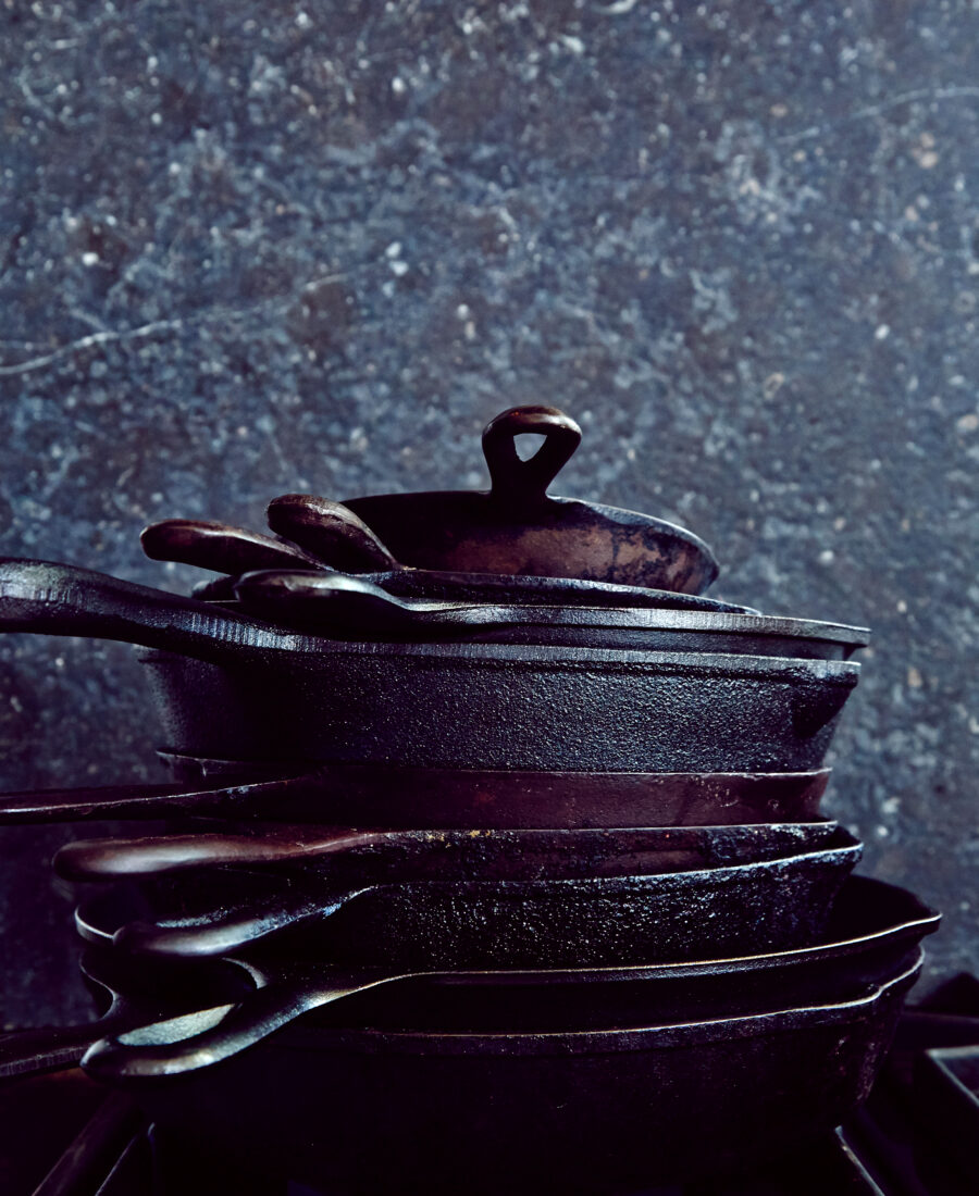 A stack of cast iron skillets and pans on a grey background