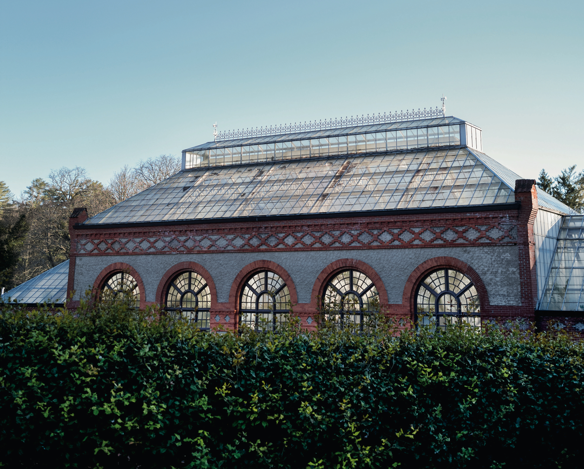 A greenhouse with a glass ceiling and window arches and hedges