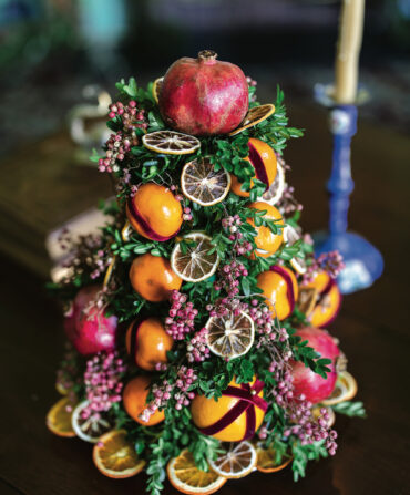 A tree-shaped decoration made of boxwood sprigs, ribbon, pomanders, dried pepperberry, and citrus slices.