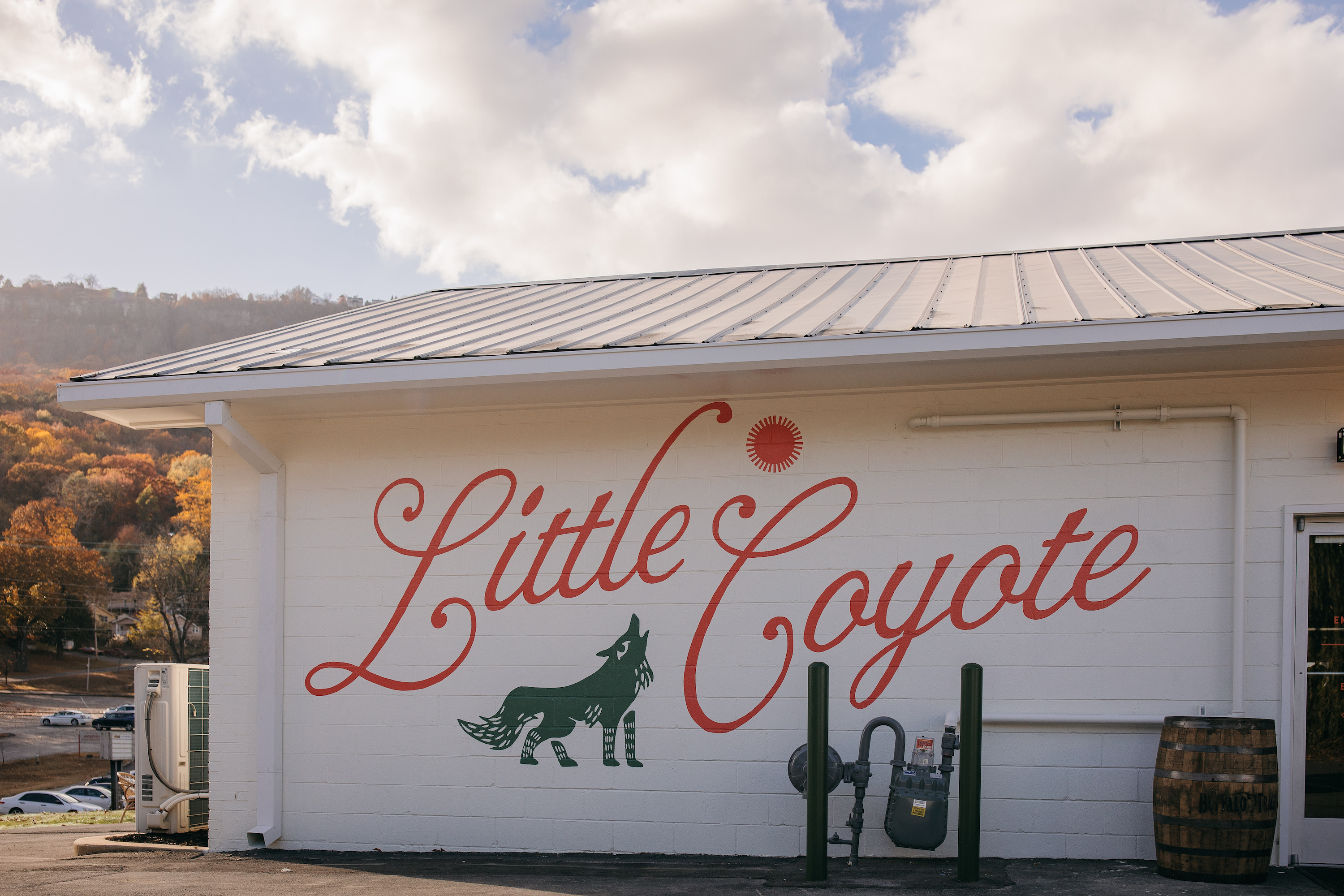 The exterior wall of a restaurant; it has "Little Coyote" painted in large red cursive letters, and a red sun and green coyote are on the wall.