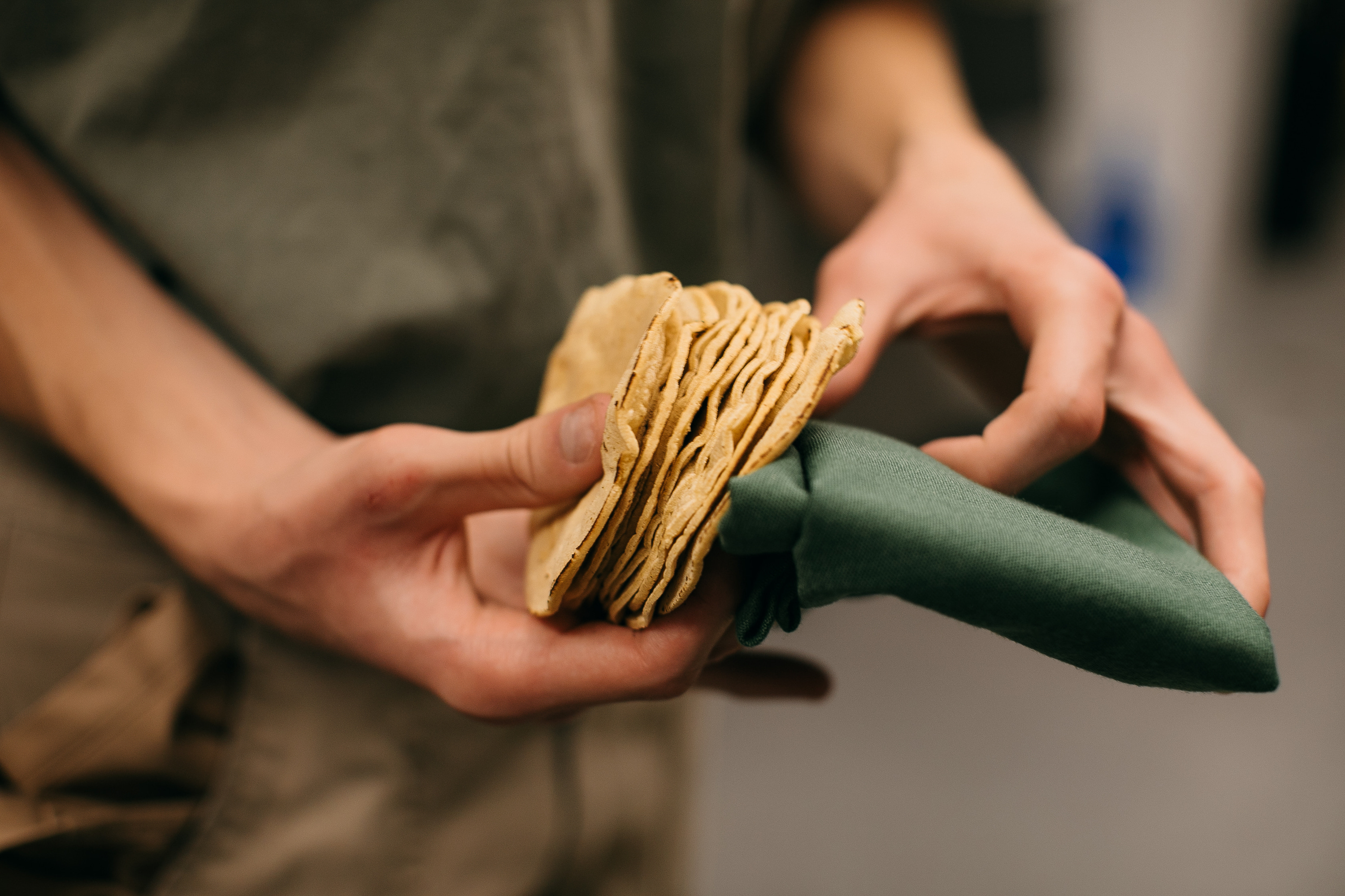 A hand holds a green cloth and a stack of tortillas