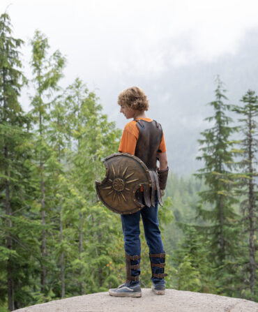 A boy stands on a rock in a forest