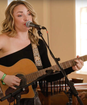 Singer Emily Curtis plays a guitar and sings into a microphone