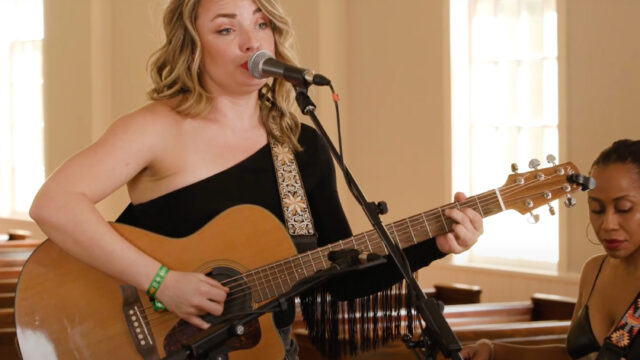 Singer Emily Curtis plays a guitar and sings into a microphone