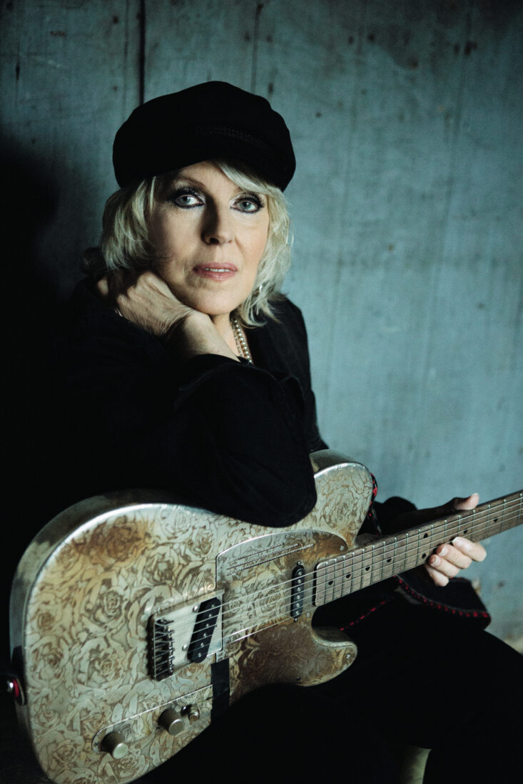 A woman with a beret wears black and holds a guitar