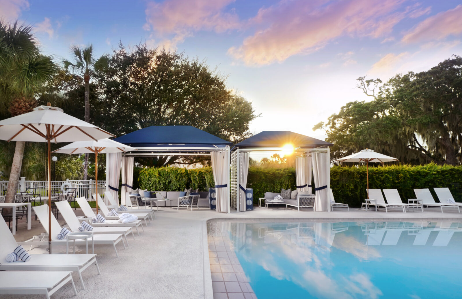 A pool with white umbrellas and a blue tent and a sky with pink clouds