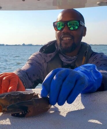 A fisherman with gloves holds a crab on top of a surface of a boat
