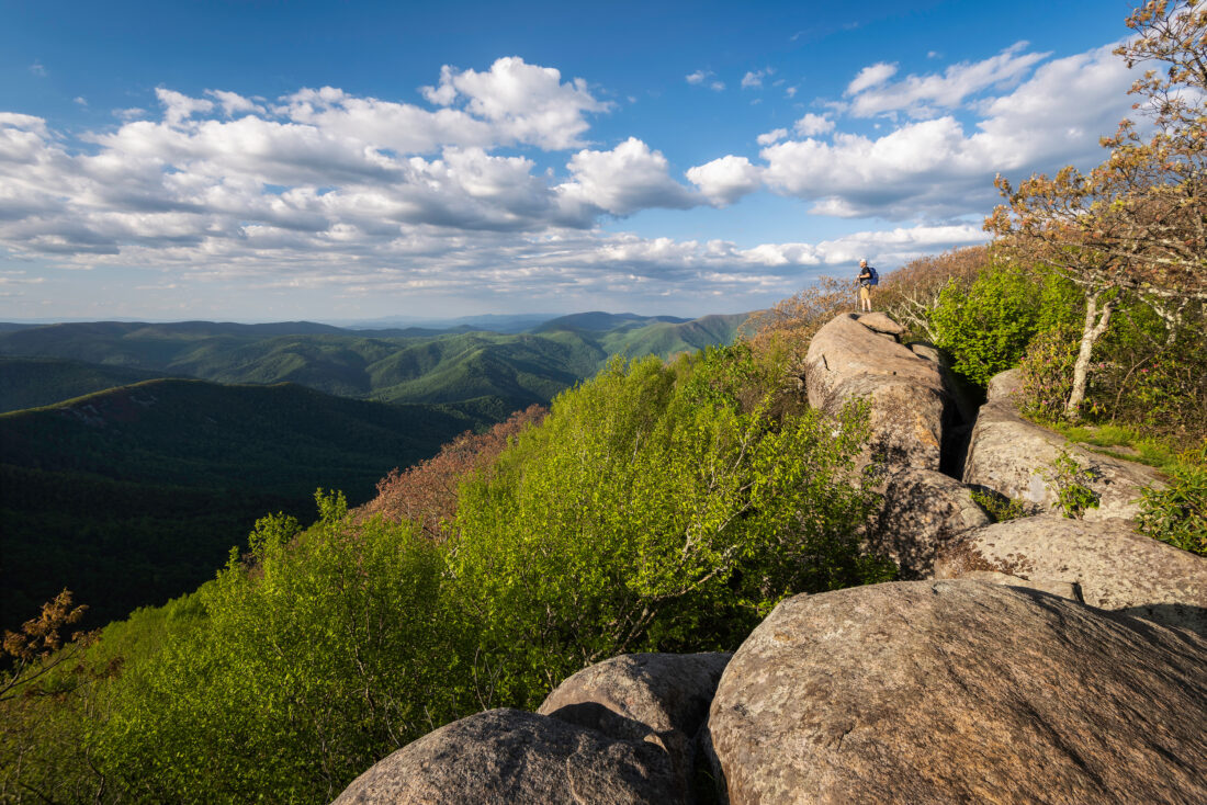 A hiker stands on a rock path and looks out over a mountainscape