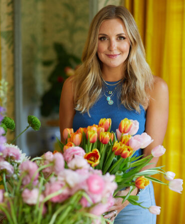A woman in a blue top and blonde hair holds a bouquet of yellow and red tulips