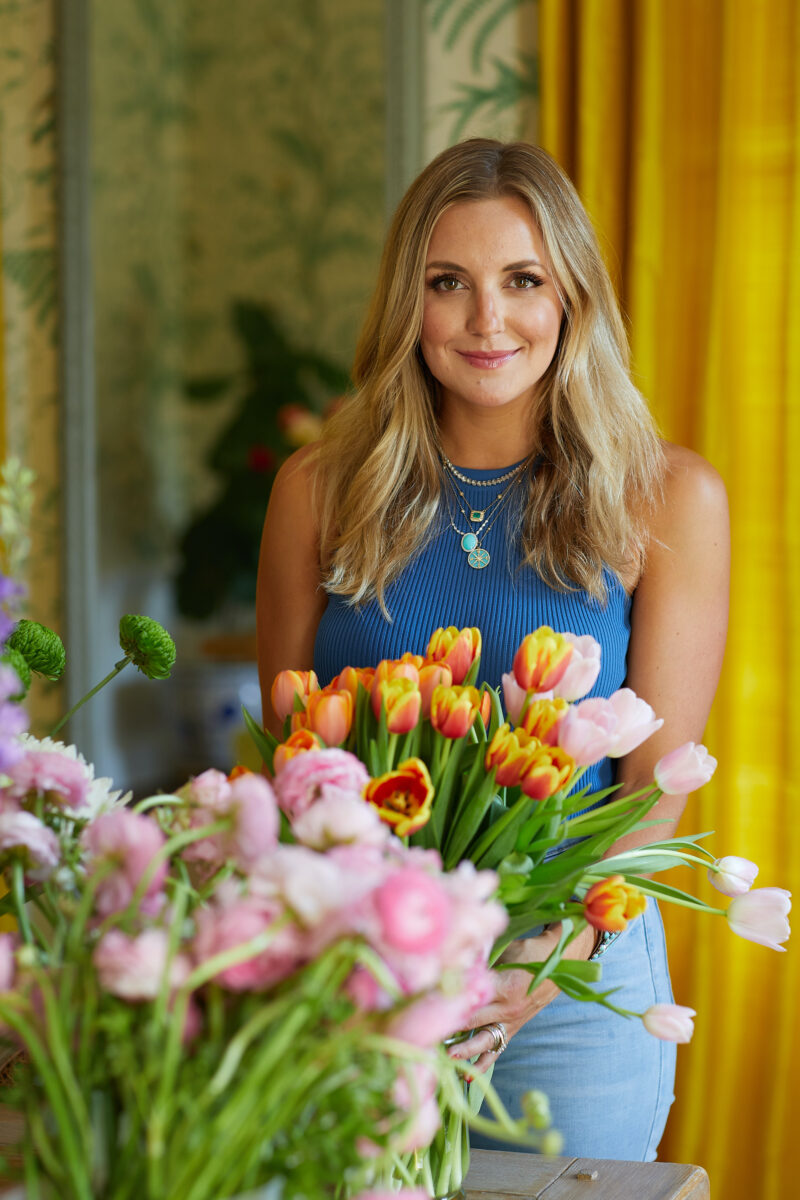 A woman in a blue top and blonde hair holds a bouquet of yellow and red tulips