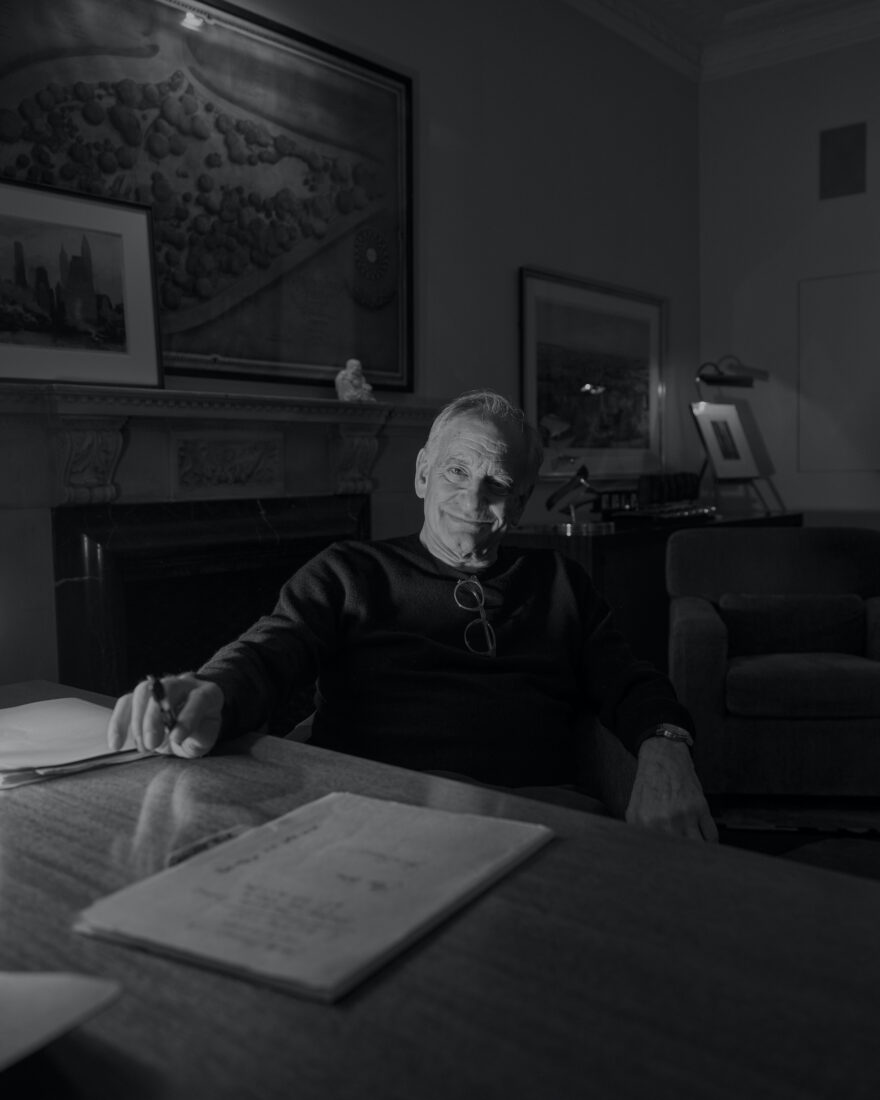 A black and white photo of a man sitting at a writing desk with a pen in his hand and a writing pad on the table