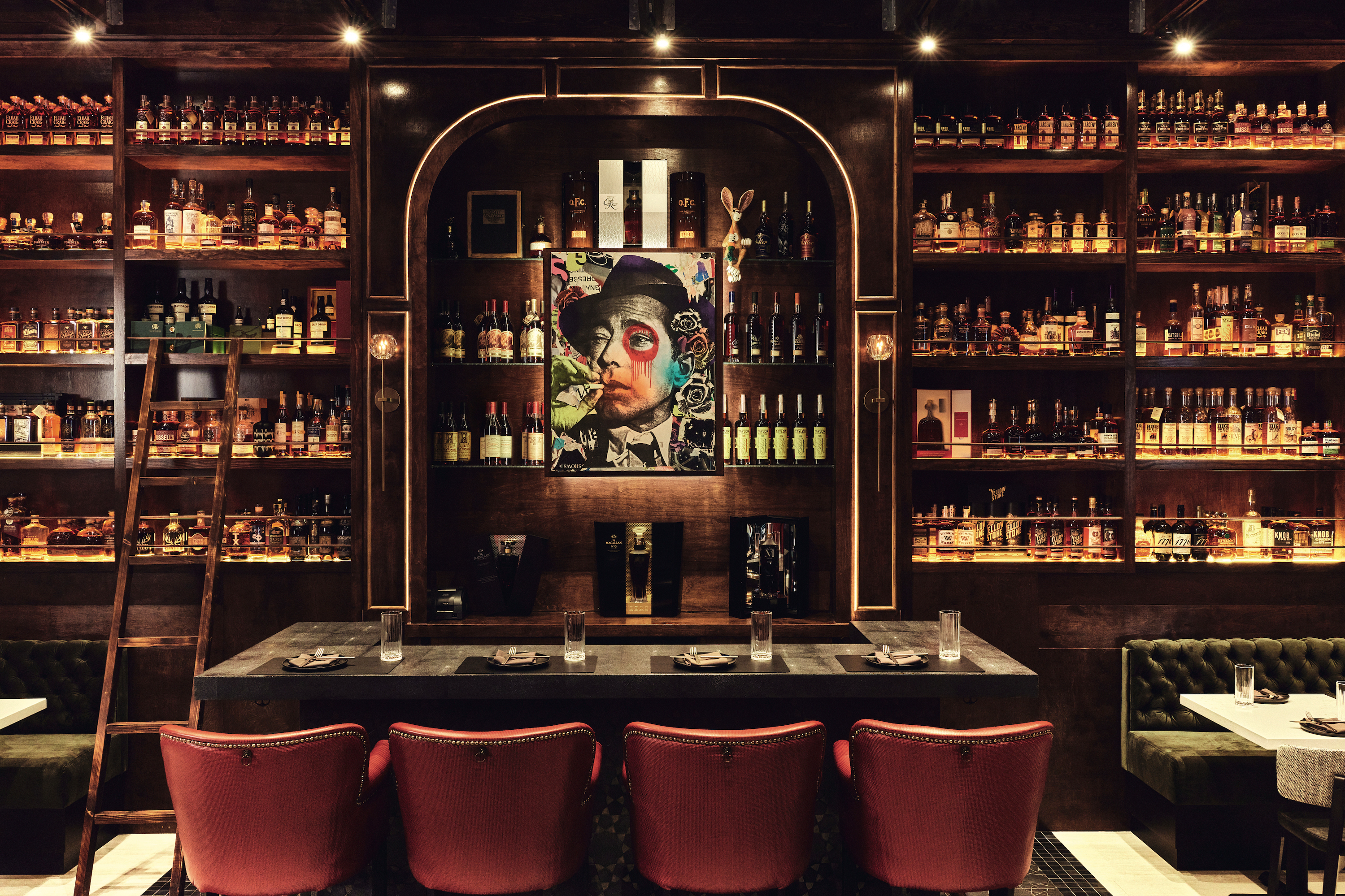 A whiskey bar with a painting of a man in the middle leather seats, many bottles, and warm lighting