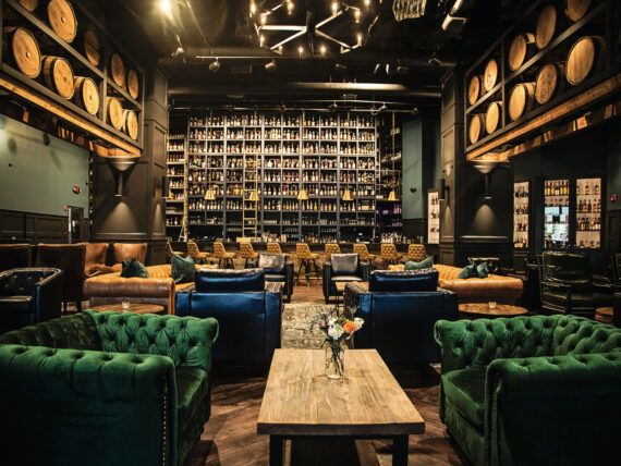 Inside a dark, elegant bourbon bar with velvet green chairs, leather sofas, and a tall bar with a ladder