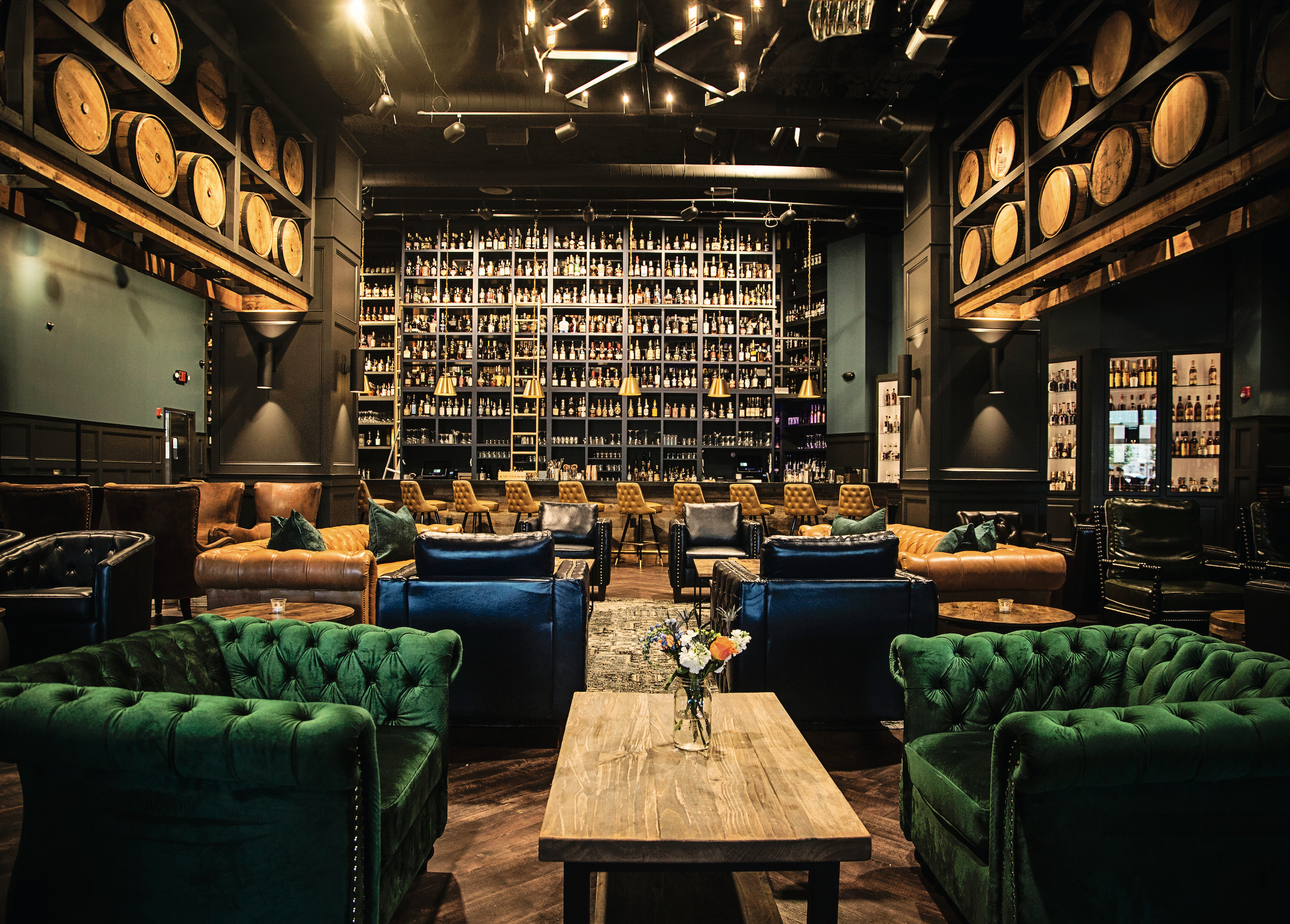 Inside a dark, elegant bourbon bar with velvet green chairs, leather sofas, and a tall bar with a ladder