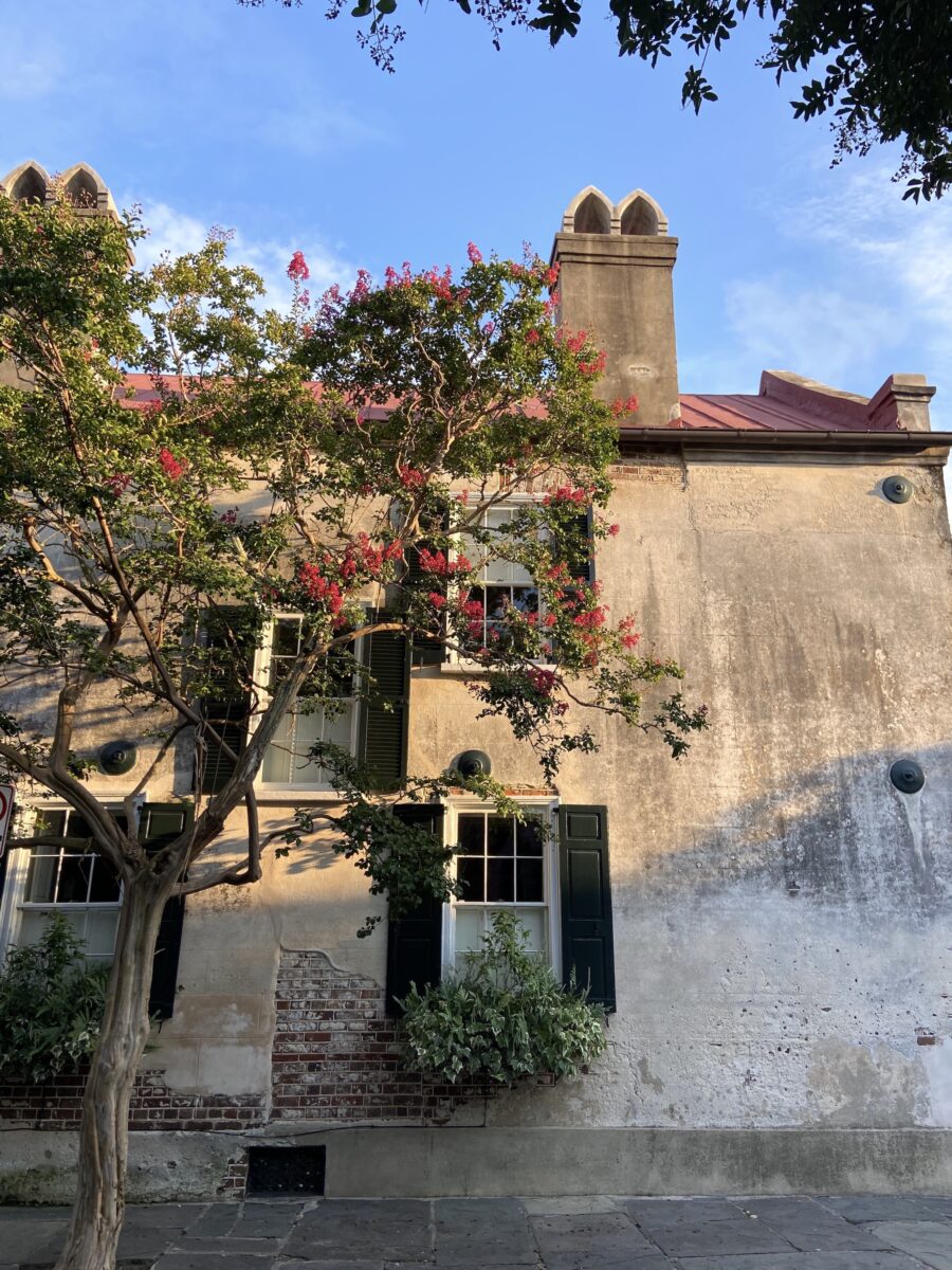 The side of a stone house with large windows and a crepe myrtle in bloom