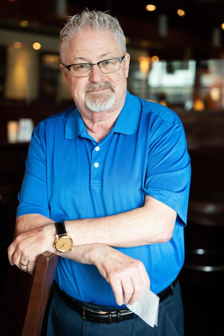 Mike Shine wearing a blue polo shirt, standing with his arms crossed.